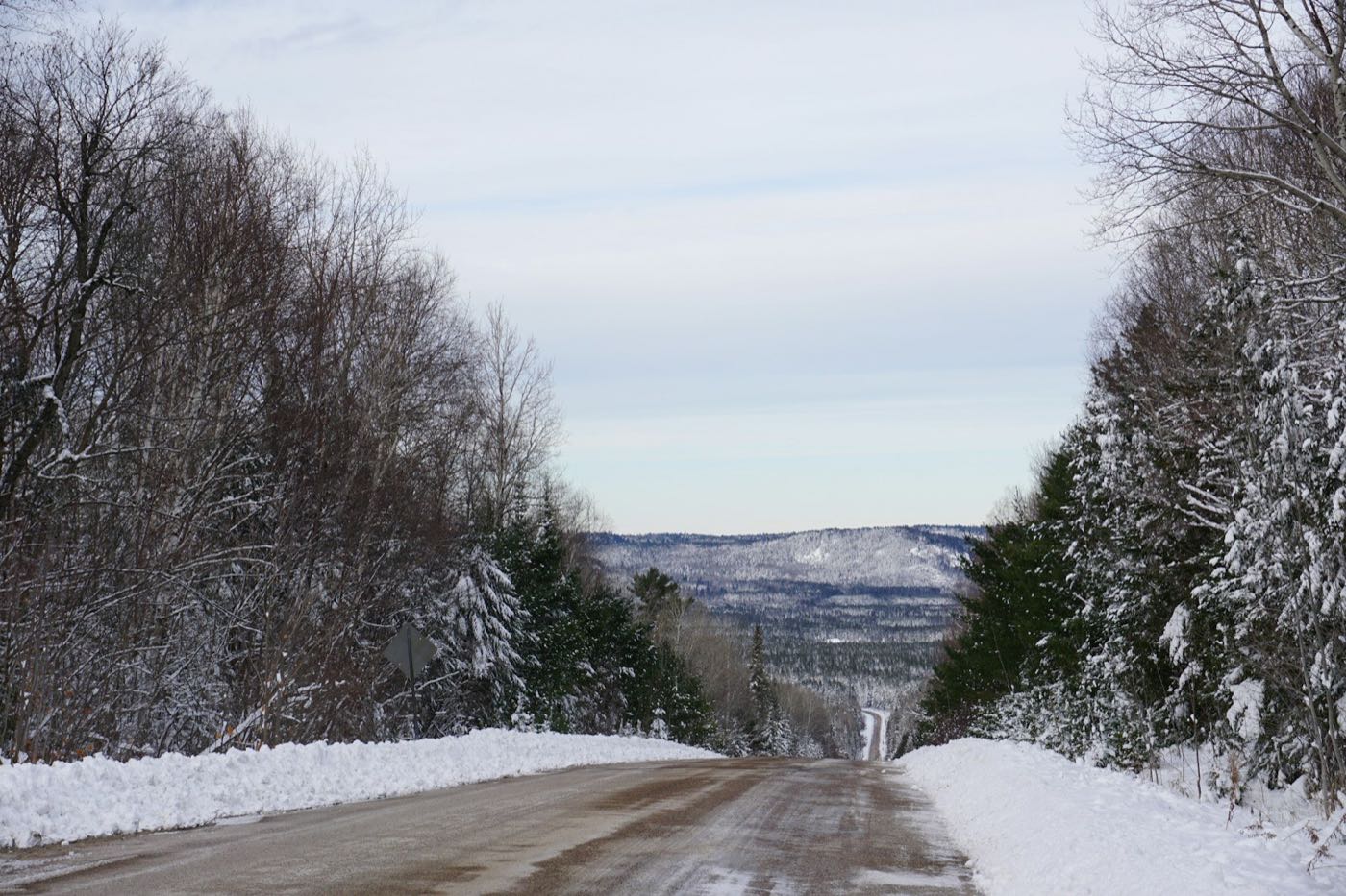 A snowy highway descending through forest toward distant hills