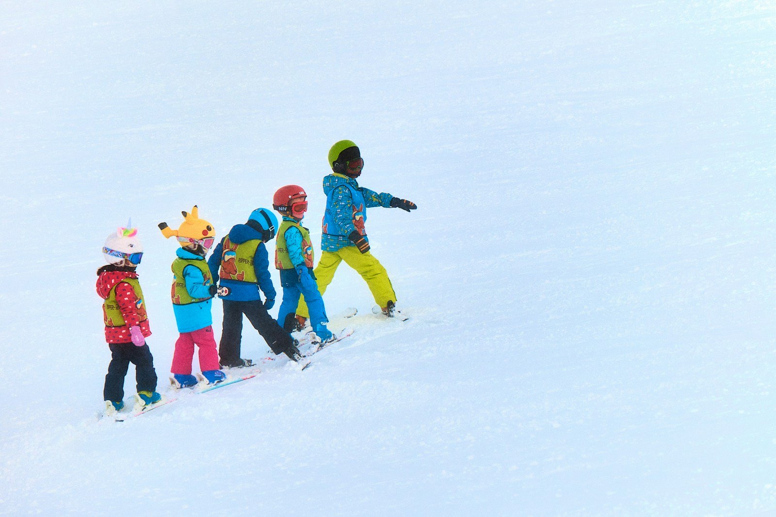 A line of young kids in bright helmets learning to ski